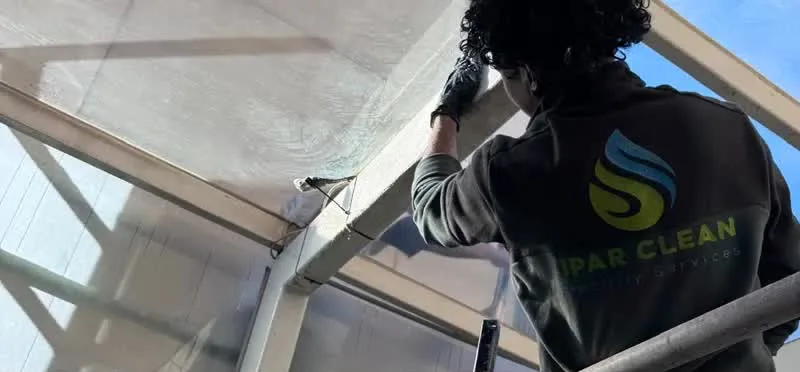 Operario de Ipar Clean limpiando la estructura acristalada de la salida de un parking en Indautxu, Bilbao